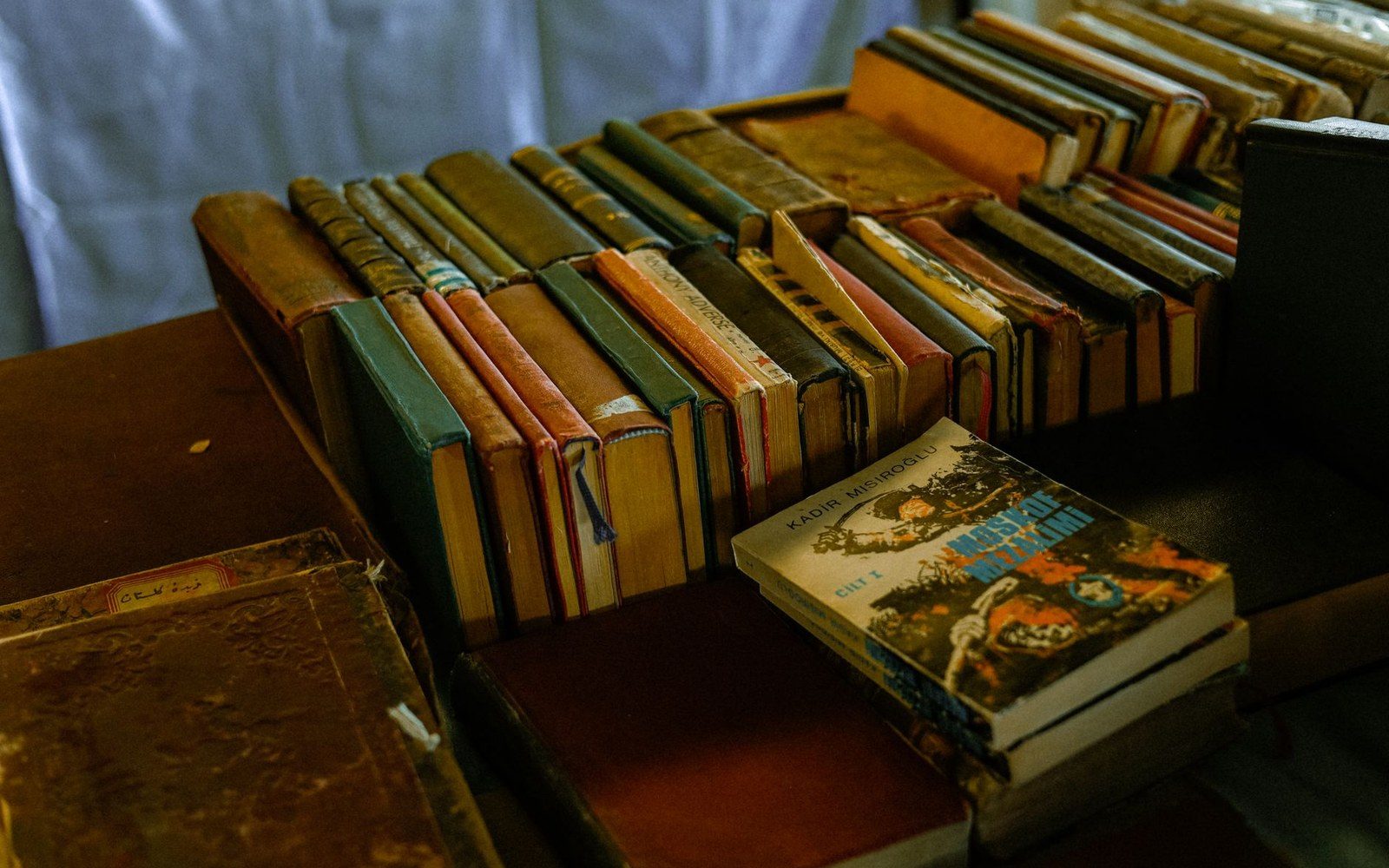 Rows of worn hardcover books stacked on a table beside a paperback with illustrated cover