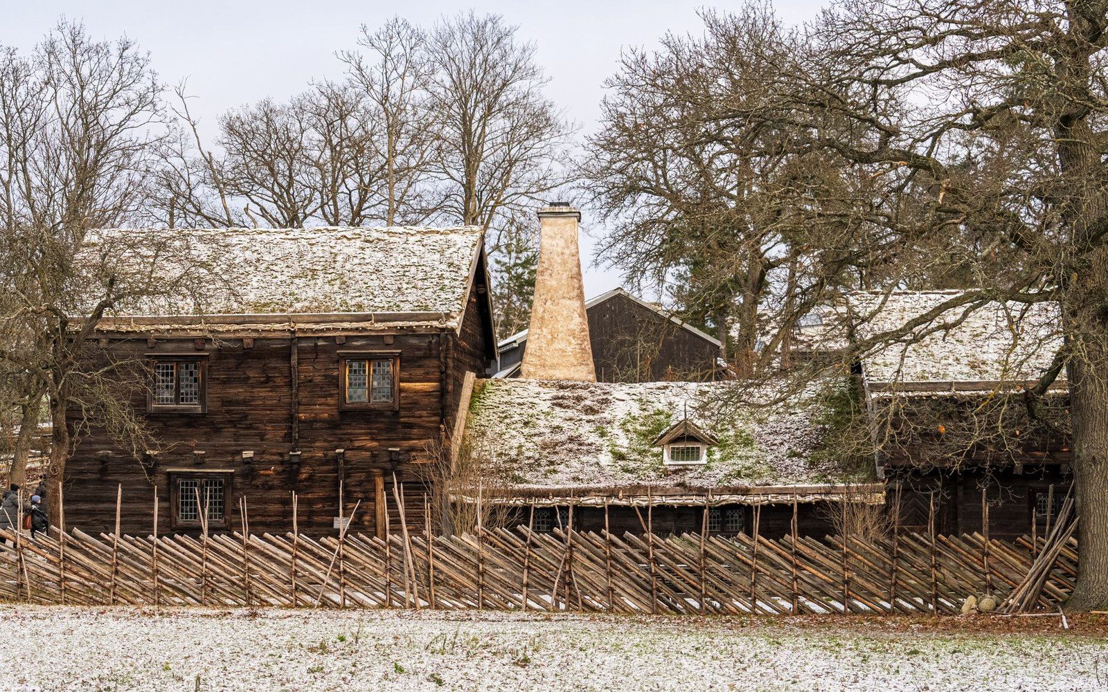 Snow dusts the roofs of old timber buildings behind a wooden picket fence
