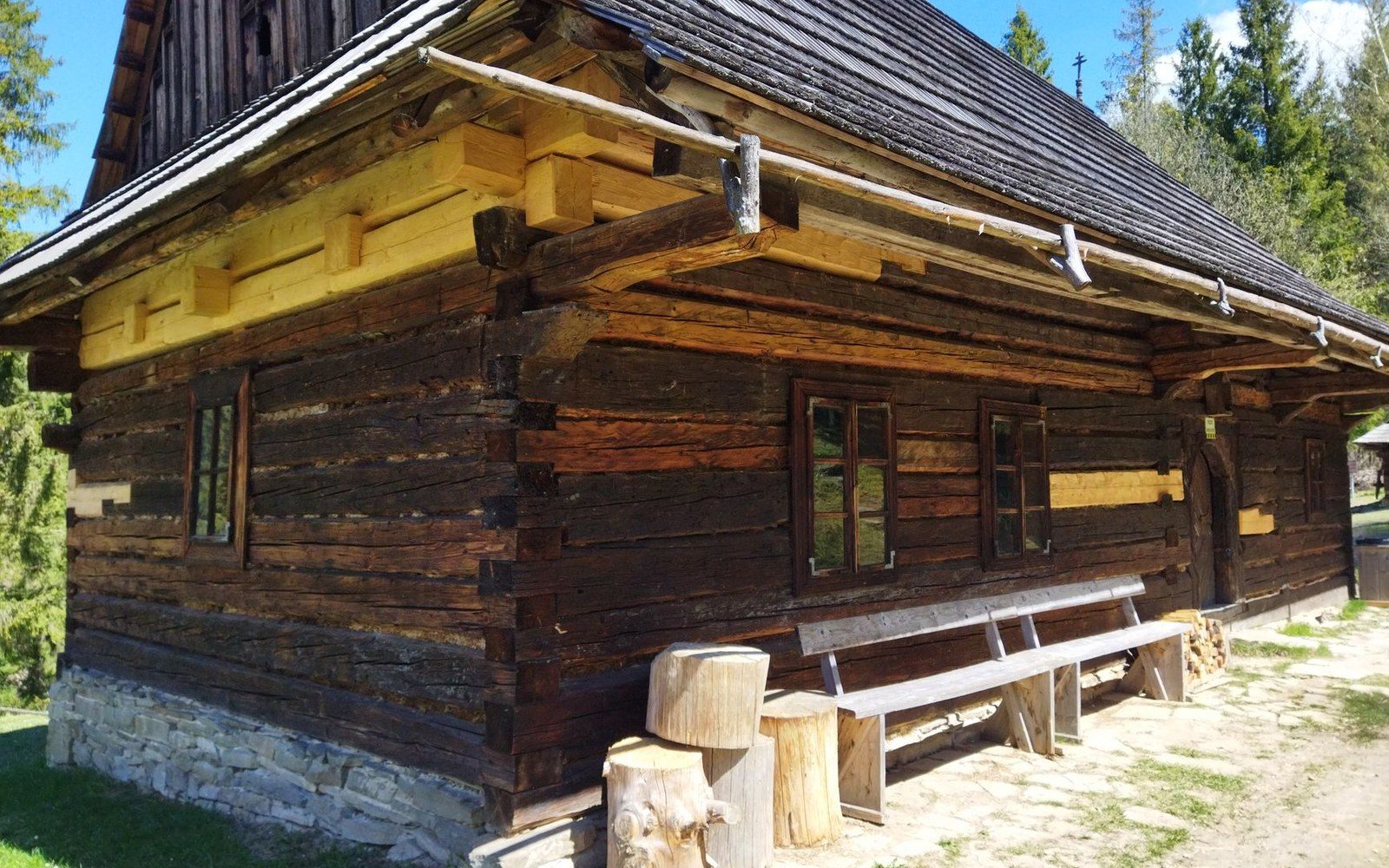 Wooden log cabin with a shingled roof and a bench along its stone-based wall