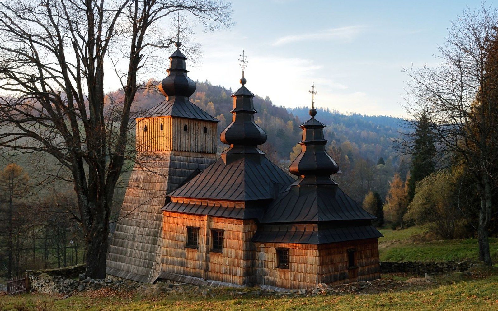 Wooden tserkva with three onion-domed towers surrounded by forested hills