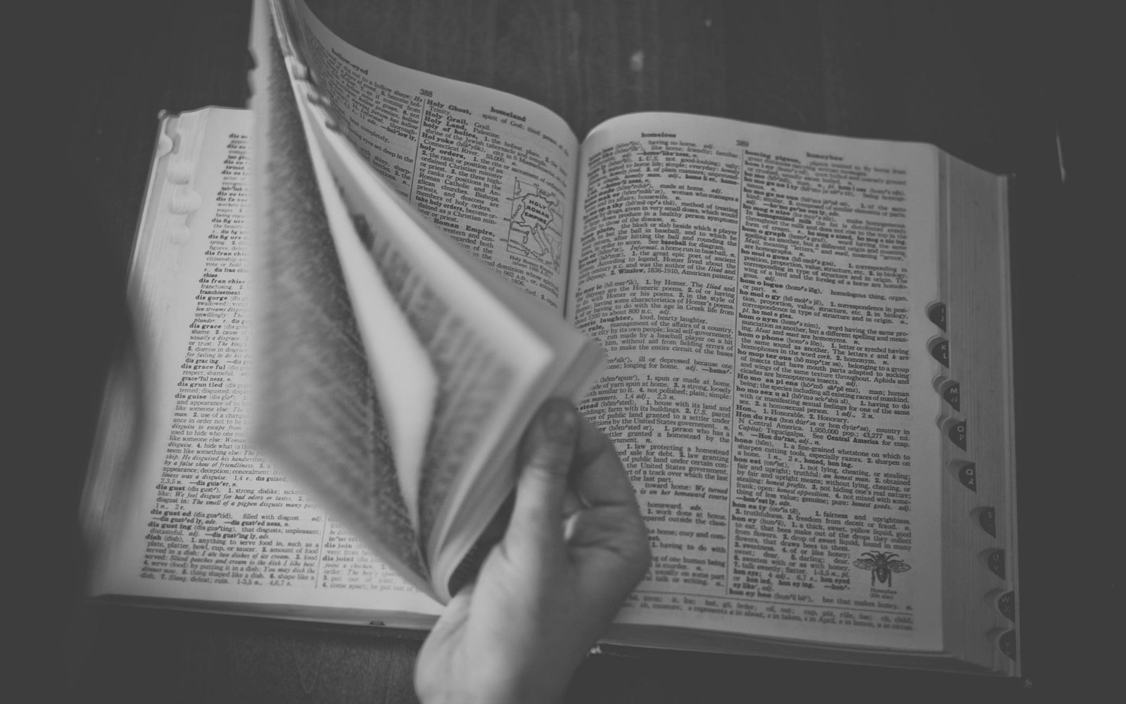 A hand flips through pages of a large dictionary with thumb-index tabs
