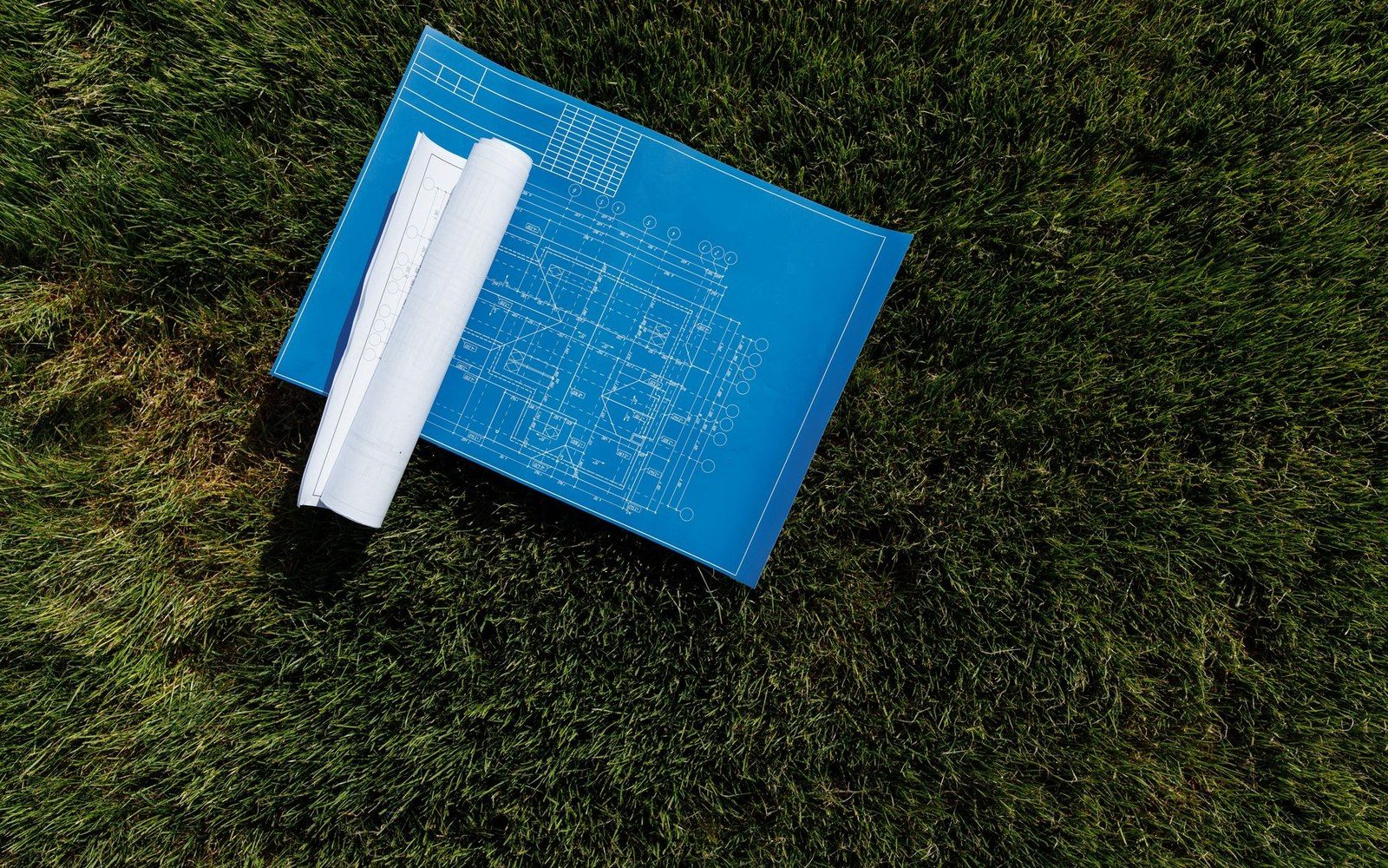 A rolled architectural blueprint with a floor plan lies on grass