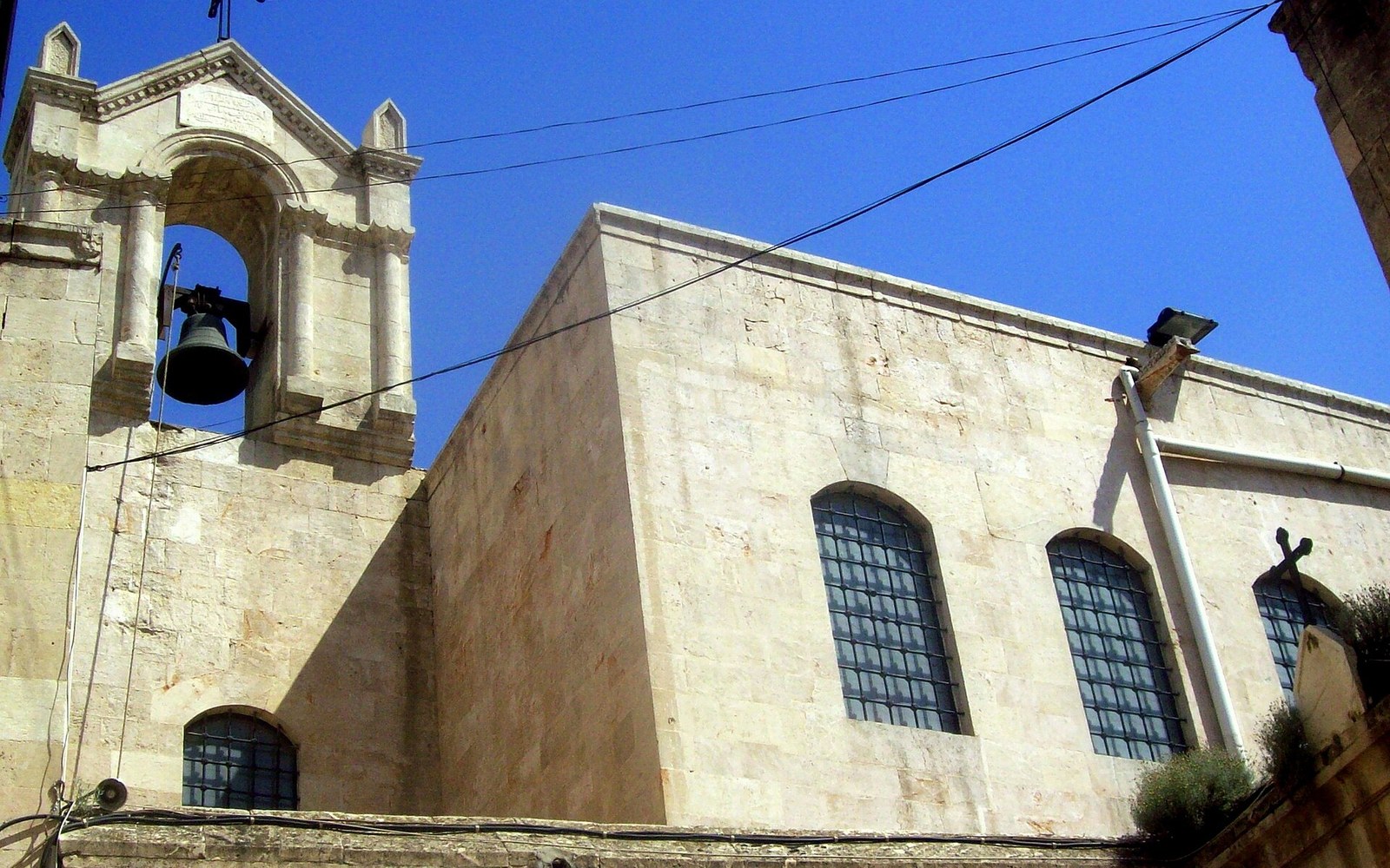Stone church facade with arched bell tower and grated windows against a clear sky