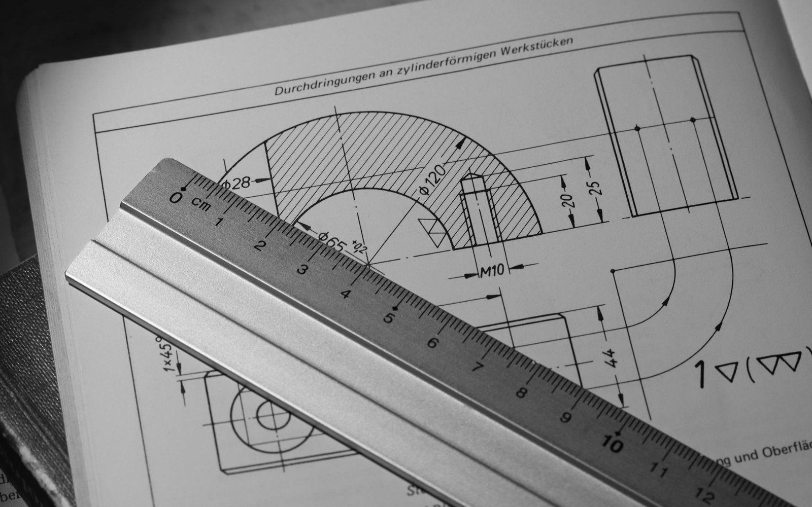 A metal ruler rests on a technical drawing showing cylindrical machine part dimensions