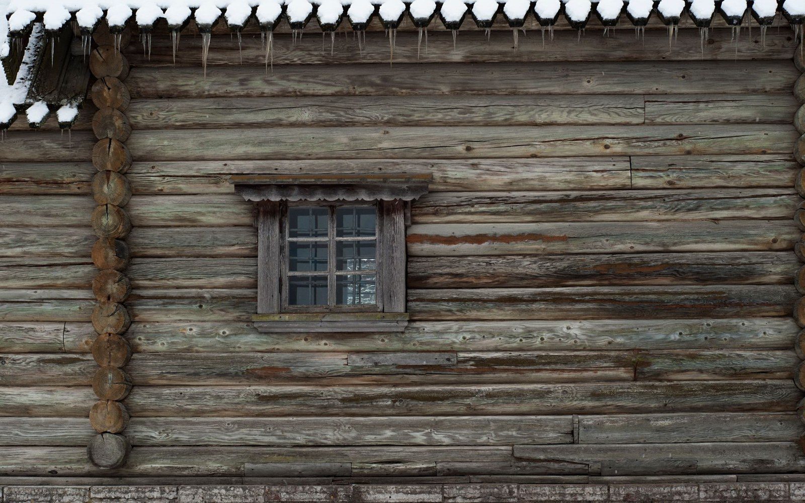 Small carved window frame set into a weathered log cabin wall with icicles above