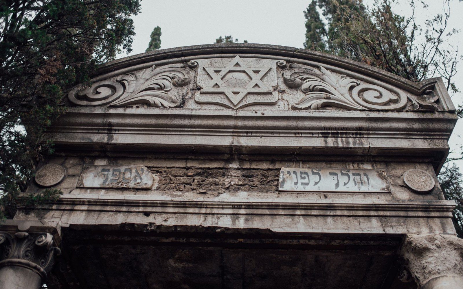 A carved matzevah stone in the Zabłudów Jewish cemetery, the relief carving in sharp focus, flat fields in the background